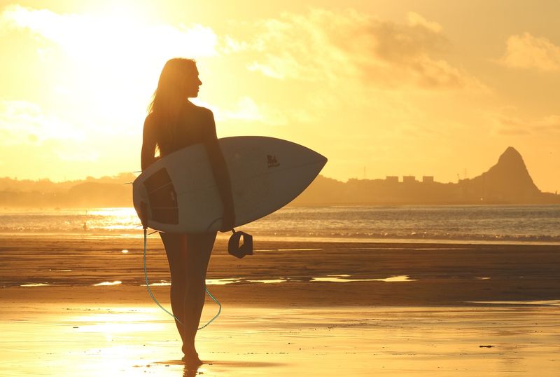 Nainen rannalla surffilauta kädessään